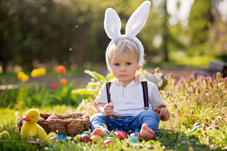 Sweet toddler boy with bunny ears, egg hunting for Easter, child and Easter day traditions. Kids and holidaysの写真素材