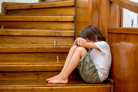 Sad child, sitting on a staircase in a big house, concept for bullying, depression stress or frustrationの写真素材