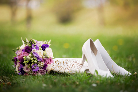 Brides wedding shoes, purs and a bouquet with roses and other flowers on the grass in the parkの写真素材