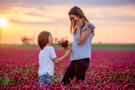 Beautiful kid and mom in spring park, flower and present. Mothers day celebration concept. Mom and son in crimson clover field, mom getting bouquet of flowers gathered from her child for Mothers dayの写真素材