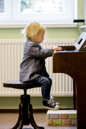 Small toddler boy enjoys playing piano for the first time, having funの写真素材