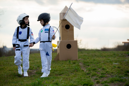 Two adorable children, boy brothers, playing in park on sunset, dressed like astronauts, imagining...