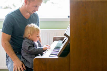Small toddler boy enjoys playing piano for the first time, having funの写真素材