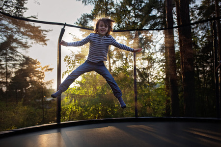 Sweet preteen boy jumping on trampoline making somersaults in the air. Child levitating. Happy child jumping on sunsetの写真素材