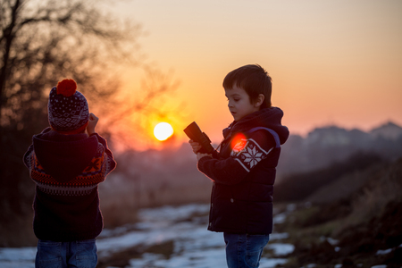 Two little children, boys, exploring nature with binoculars, looking at sunsetの写真素材