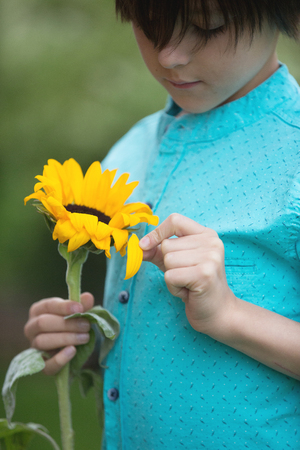 Boy holding flower in his hand on green background. European appearance, close portrait, sunflowerの写真素材