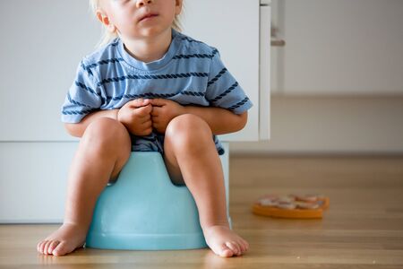 Little toddler boy, sitting on potty, playing with wooden toy at homeの写真素材