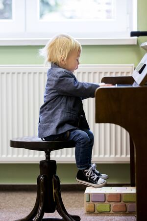 Small toddler boy enjoys playing piano for the first time, having funの写真素材