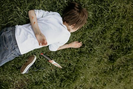 Teenager lying on the grass, covered with soil, knife next to himの写真素材