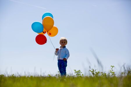 Little boy, toddler, child playing with colorful balloons in the park on kids day, sunny summer afternoon in natureの写真素材