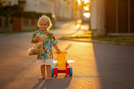 Beautiful toddler child, playing with plastic toys, blocks, cars on sunset in a small villageの写真素材