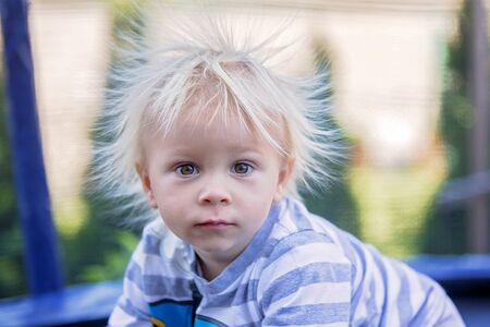 Cute little boy with static electricy hair, having his funny portrait taken outdoors on a trampolineの写真素材