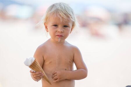 Sweet blonde toddler boy, eaiting ice cream on the beach, summertimeの写真素材