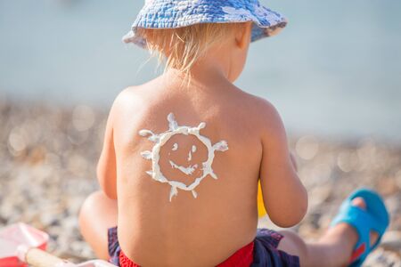 Sweet toddler child, boy, holding beach toys, with sunscream applied on his back, ready for the harsh sun on the beachの写真素材