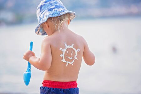 Sweet toddler child, boy, holding beach toys, with sunscream applied on his back, ready for the harsh sun on the beachの写真素材