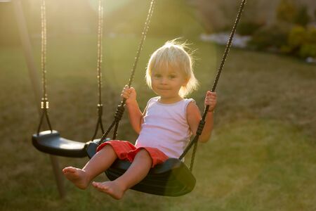 Sweet toddler child,  swinging on a swing in garden on sunset, smiling happilyの写真素材