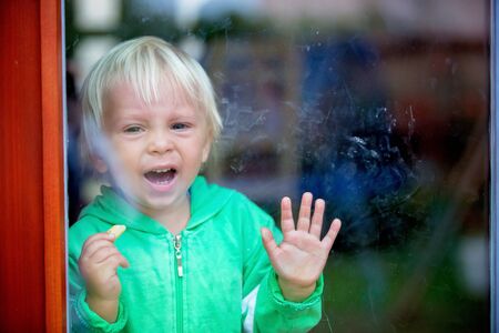 Toddle boy, crying heavily, standing in front of the door, looking at cameraの写真素材