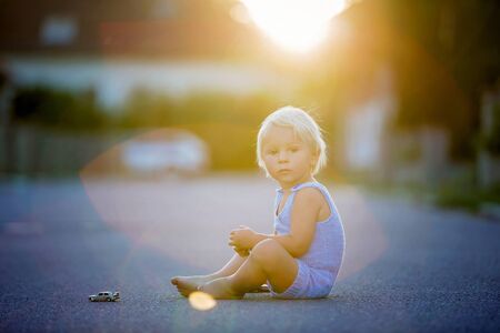 Beautiful child, playing with car toys on sunset on a quiet village street, summertimeの写真素材