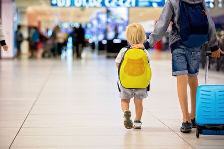 Sweet childre, brothers, boys, waking hand in hand at the airport, carrying suitcases and backpacks, family holidayの写真素材
