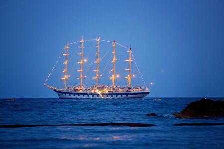 Children, sitting on beach, watching lighted ship in the ocean  on sunsetの写真素材