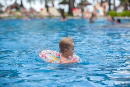 Adorable happy little child, toddler boy, having fun relaxing and playing in a pool in inflatable ring on sunny day during summer vacation in Mauritius resortの写真素材