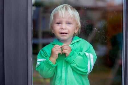 Toddle boy, crying heavily, standing in front of the door, looking at camera