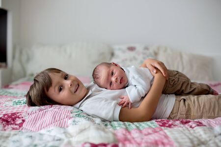 Sweet preschool boy, hugging with tenderness and care his little newborn brother at homeの写真素材