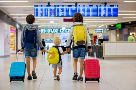 Sweet childre, brothers, boys, waking hand in hand at the airport, carrying suitcases and backpacks, family holidayの写真素材
