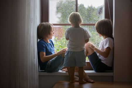 Happy siblings, boy brothers, sitting on a window shield on a rainy day, playing together, summertimeの写真素材
