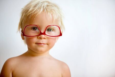 Sweet toddler boy with red eyeglasses on white background, making sweet facesの写真素材