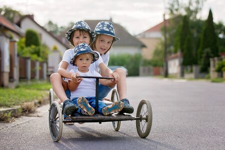 Happy children, boy brothers, riding old retro car with four wheels in a villageの写真素材