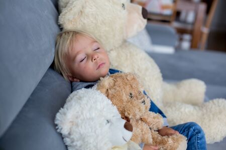 Blond toddler boy, sleeping with many teddy bears in the afternoon on the sofa