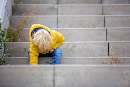 Blonde little toddler child in yellow jacket, playing on the playground, autumn sunny day