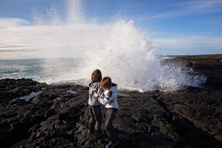 Children watching gig waves crashing in rocks on the south west coast on Iceland, near Gunnuhver