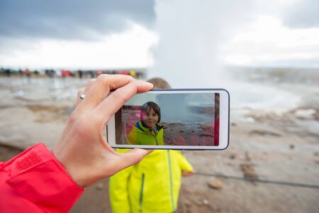 Mother recording video of her preschool son, boy enjoying the eruption of Strokkur Geysir in Iceland autumntimeの写真素材