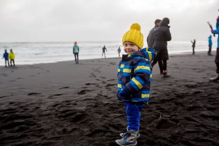 Toddler playin on black sand beach of Reynisfjara and the mount Reynisfjall in Iceland on a cold winter rainy dayの写真素材