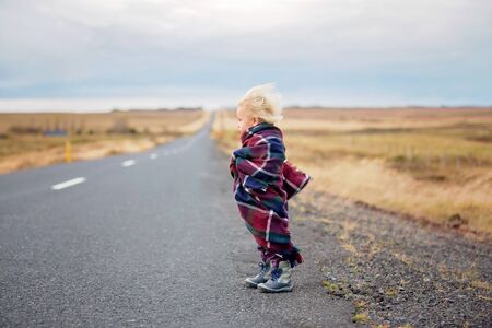 Beautiful child, standing on a road on a very windy day, wrapped in scarf, watching the sunrise in Iceland, autumntimeの写真素材