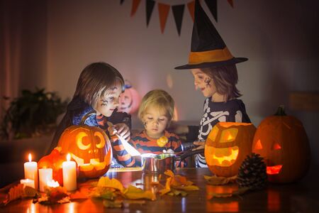 Children, boy brothers, playing with carved pumpkin at home on Halloween, making magic potionの写真素材