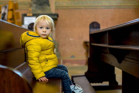Toddler child sitting on a praying bench in churchの写真素材