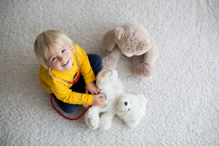 Sweet toddler child, playing doctor, examining teddy bear toy at home, isolated backgroundの写真素材