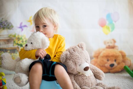 Cute toddler boy, potty training, playing with his teddy bear on pottyの写真素材