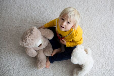 Sweet toddler child, playing doctor, examining teddy bear toy at home, isolated backgroundの写真素材