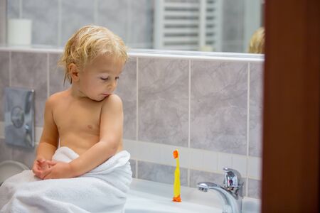 Sweet toddler boy, brushing his teeth in bathroom in the evening after taking a bathの写真素材
