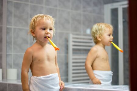 Sweet toddler boy, brushing his teeth in bathroom in the evening after taking a bathの写真素材