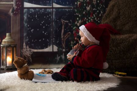 Sweet toddler boy, reading book at home at night on Christmas nightの写真素材