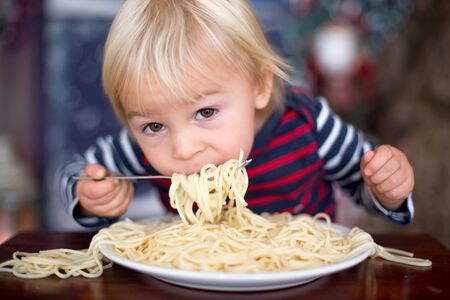 Sweet toddler child, boy, eating spaghetti at home on Christmasの写真素材