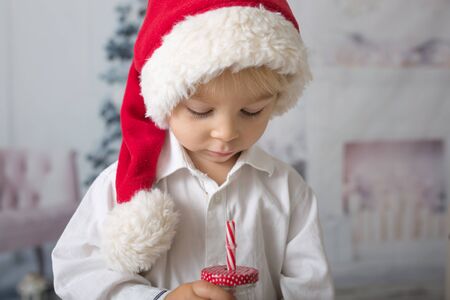 Beautiful toddler boy with red santa hat, holding bottle with milk, drinking, Christmas decoration
