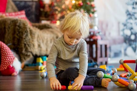 Sweet blonde toddler boy, playing with plastic construction, making different shapes, christmas decoration around himの写真素材