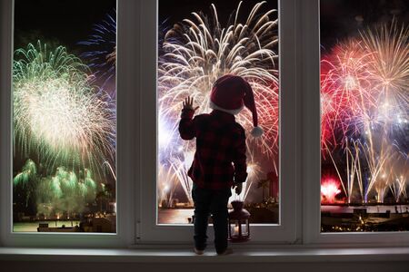 Toddler child standing in front of a big french doors, leaning against it looking at new years eve...