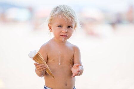 Sweet blonde toddler boy, eaiting ice cream on the beach, summertimeの写真素材